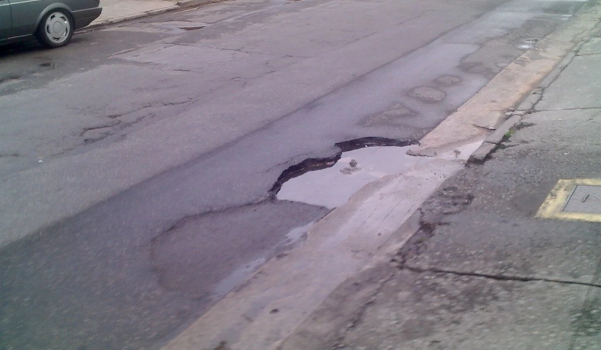 Imagem com uma rua com um buraco grande próximo à guia, paralelepípedo.