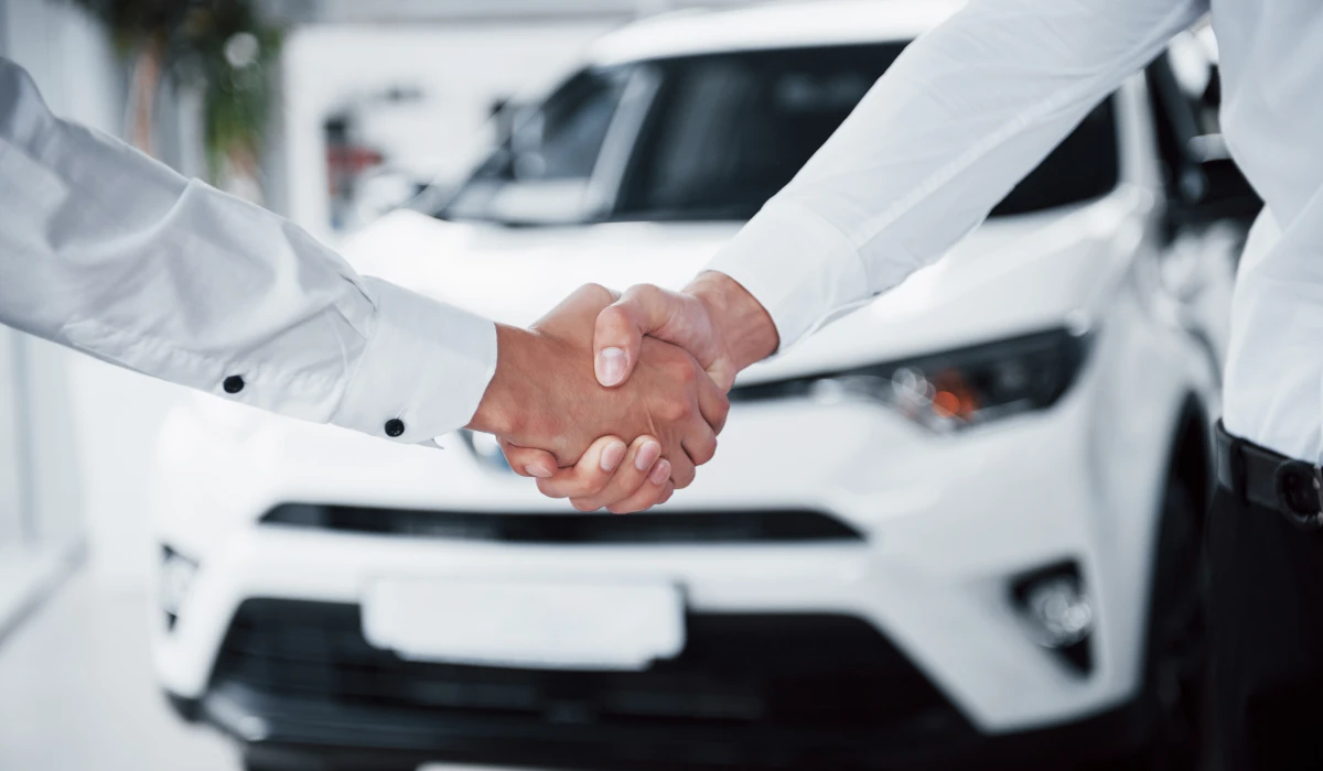 Imagem com duas pessoas dando as mãos por terem efetuado uma compra de um veículo