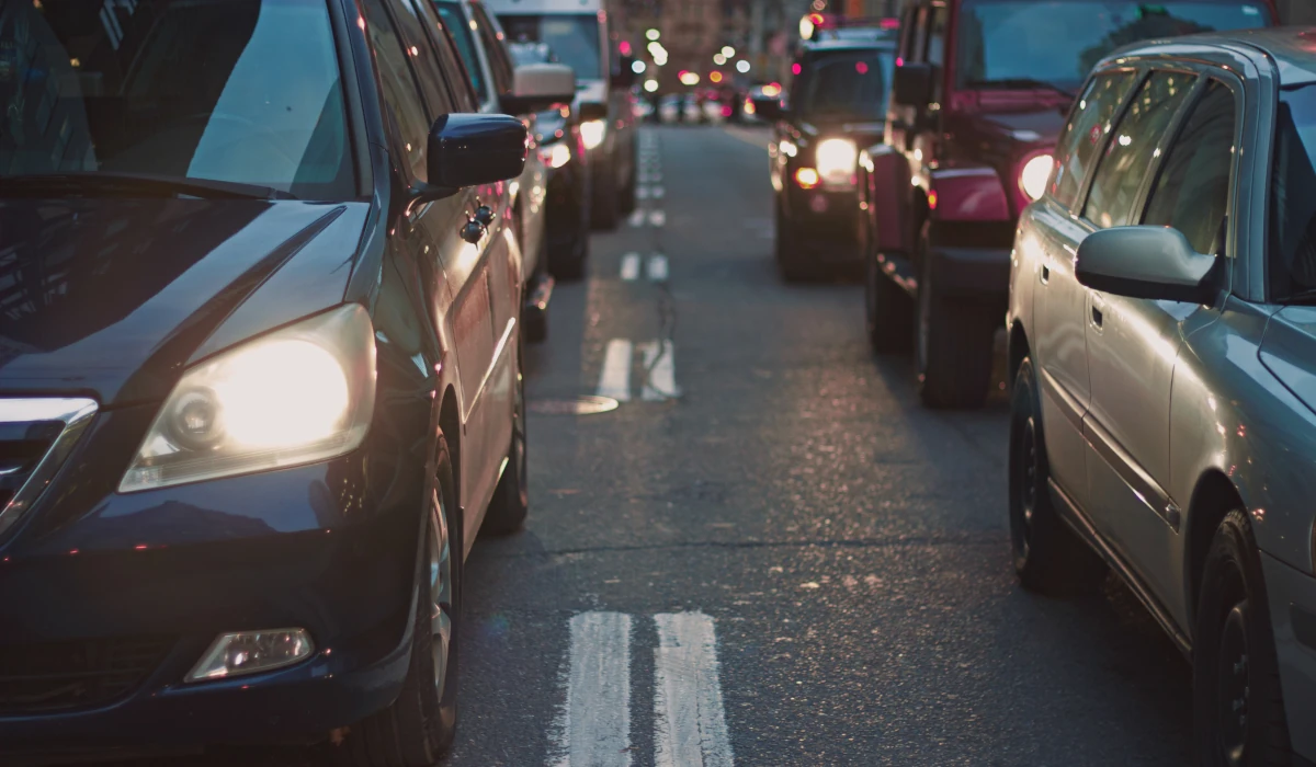 Imagem tirada em pé em uma rua com carro nela andando devagar por alto volume de carros