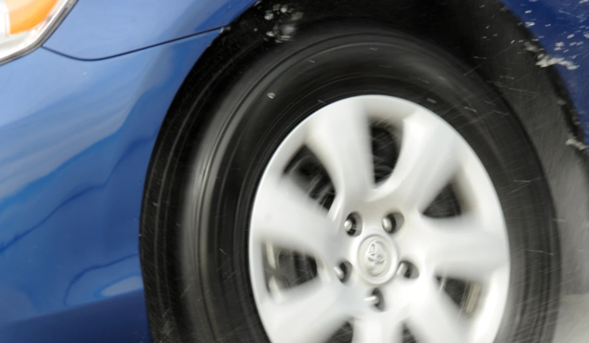 Imagem de um pneu na roda de um veículo girando uma via com água para destacar a manutenção para aumentar a vida útil do pneu