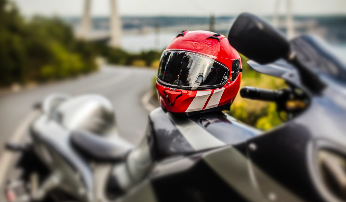 Foto de um capacete apoio na tanque de uma moto e um cenário de estrada atrás